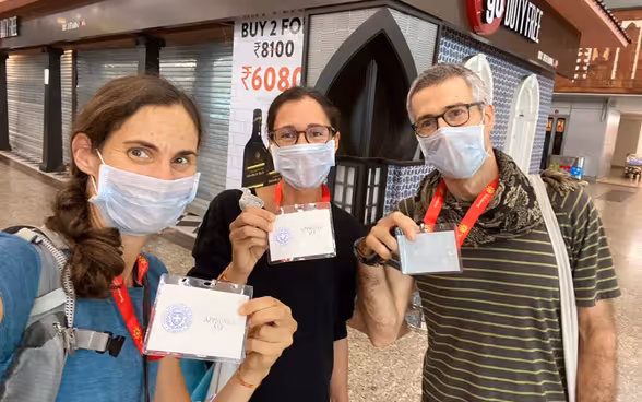 Three passengers wearing masks proudly display their Indian customs clearance badges to board the next flight to Switzerland. 