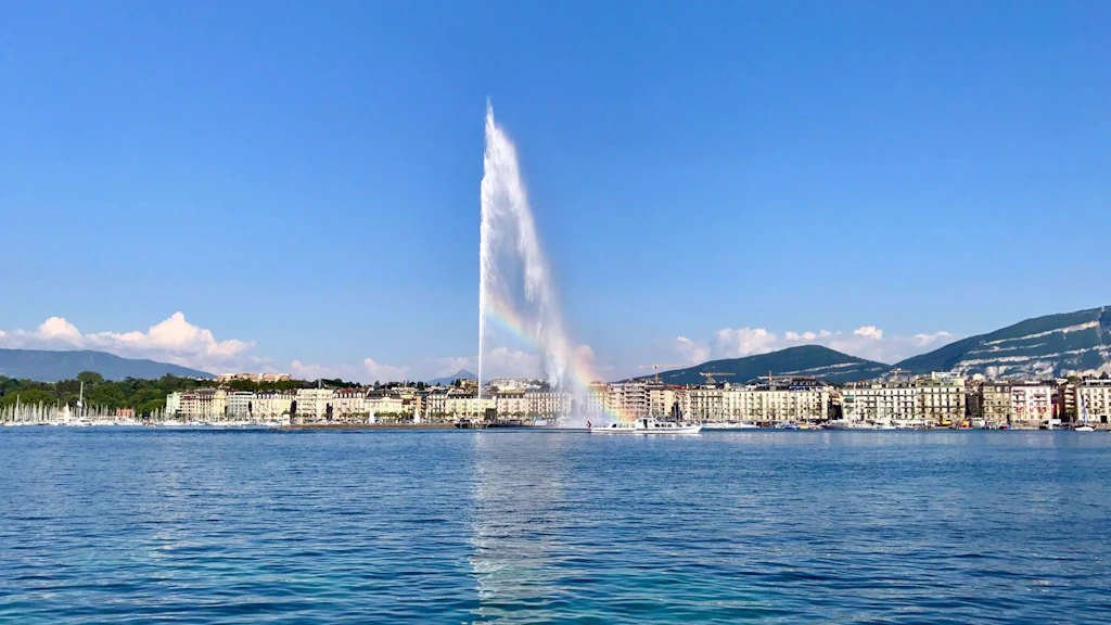 The Jet d’Eau water jet in Lake Geneva, soaring high into the blue sky, with mountains in the background.