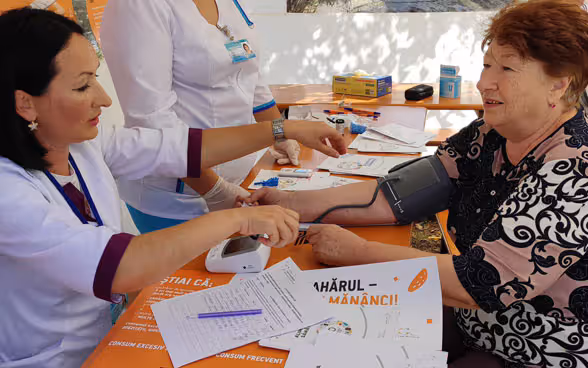 A woman measures the blood pressure of another woman sitting opposite her.