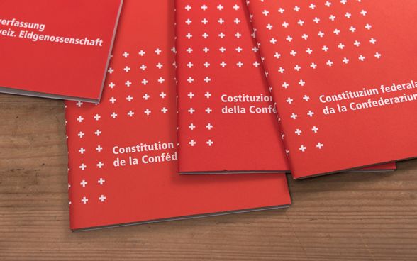 Four versions of the Swiss Federal Constitution in all four national languages on a wooden surface.
