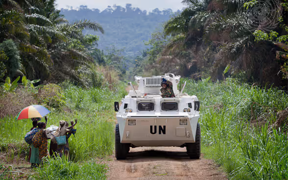 A white armoured vehicle drives through the jungle in an African country.