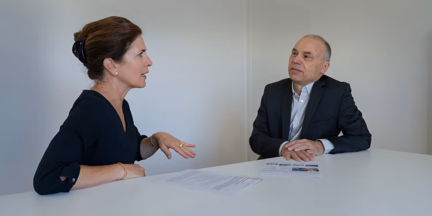 Debora Kern and Daniel Birchmeier seated at the same table, looking at some papers and engaged in animated discussion.