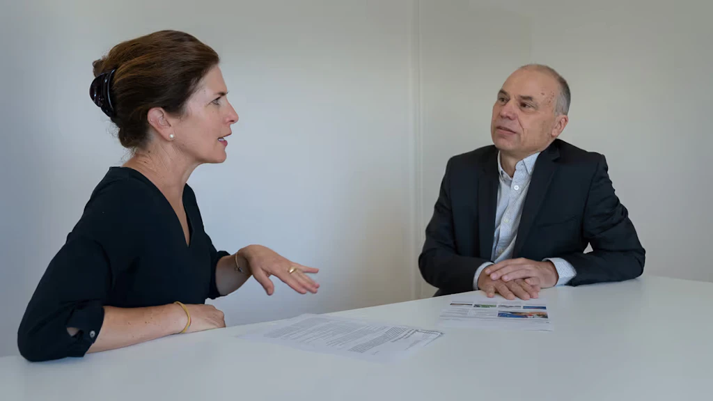 Debora Kern and Daniel Birchmeier seated at the same table, looking at some papers and engaged in animated discussion.