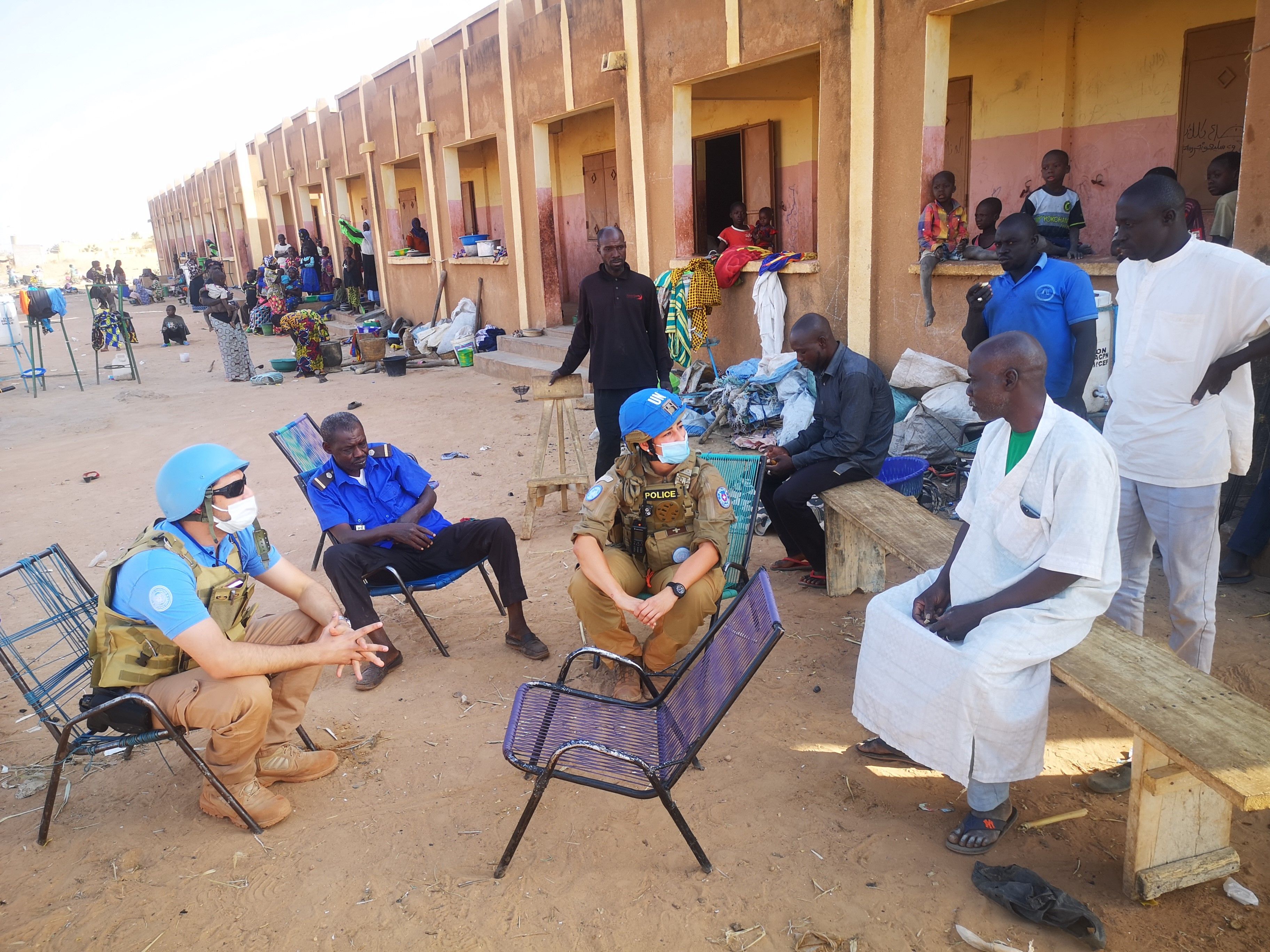 Men, women and children outside a building; in the foreground a policewoman and policeman are talking to two locals.