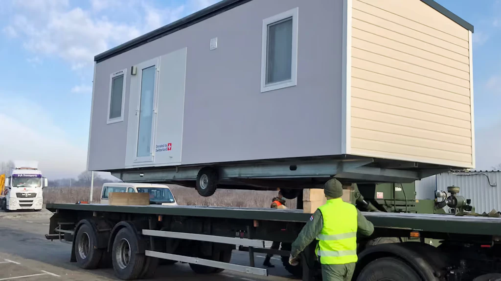 A mobile housing unit is transported by truck.