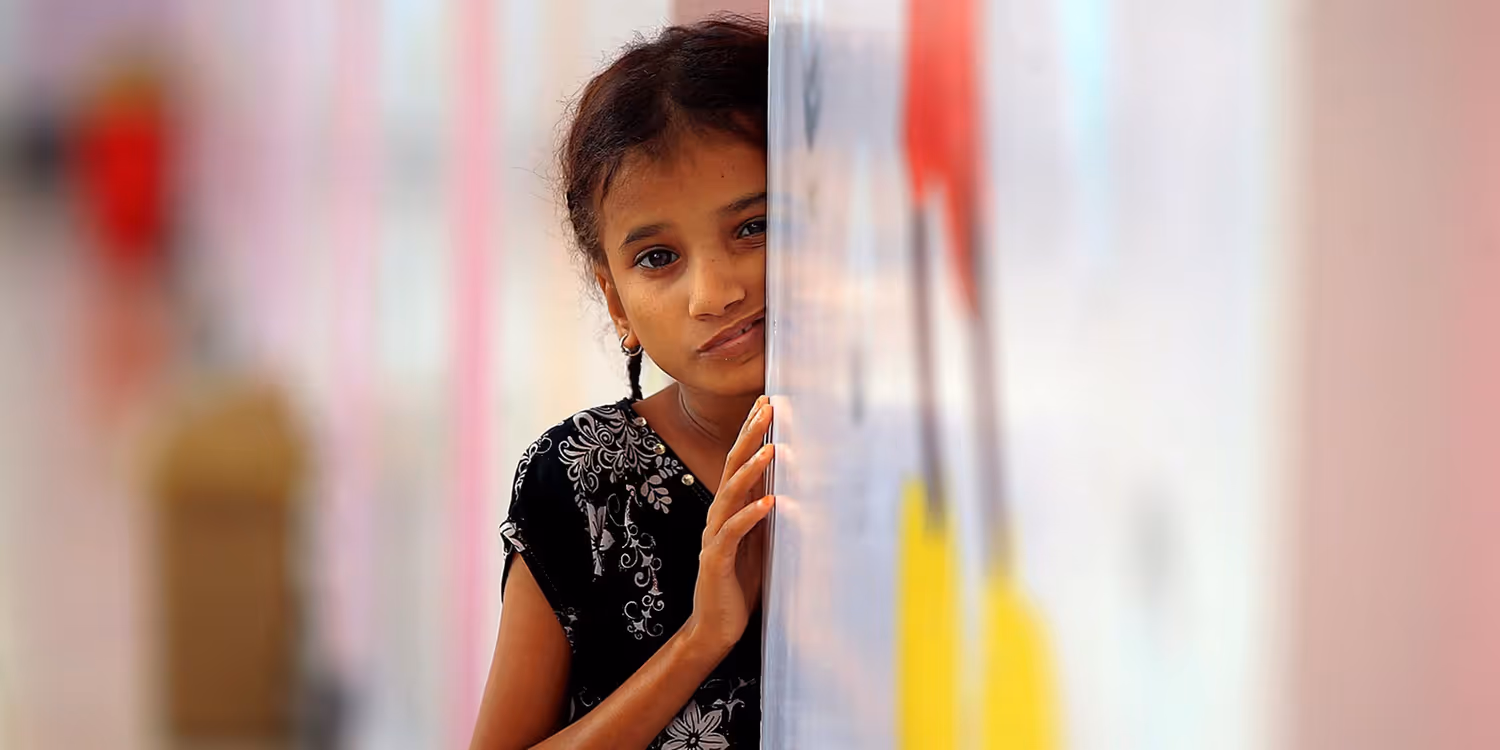 A little girl, with a worried look on her face, is leaning against a wall waiting for food.