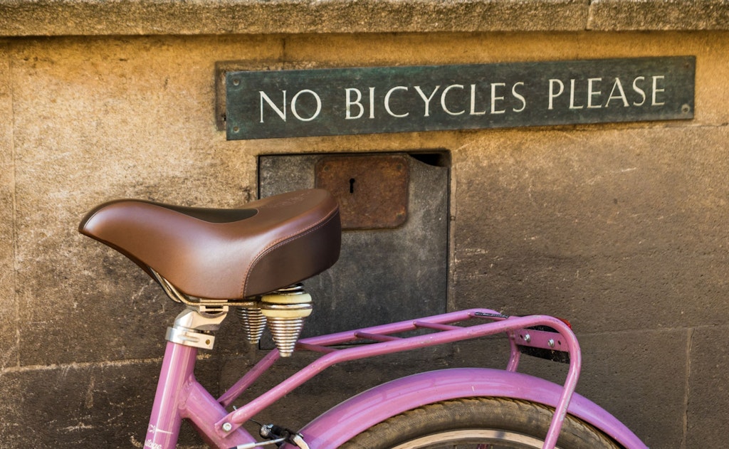 A pink bike against a wall with a sign reading ‘No bicycles please’ in capital letters.