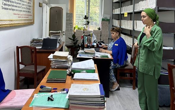 Two women are in an office with shelves full of paper.