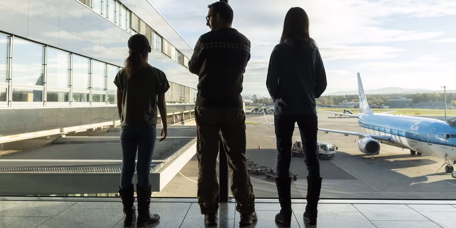 At the airport, two children and an adult are standing by the window.