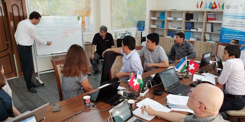 Women and men look at a white board and listen to a man's explanations.