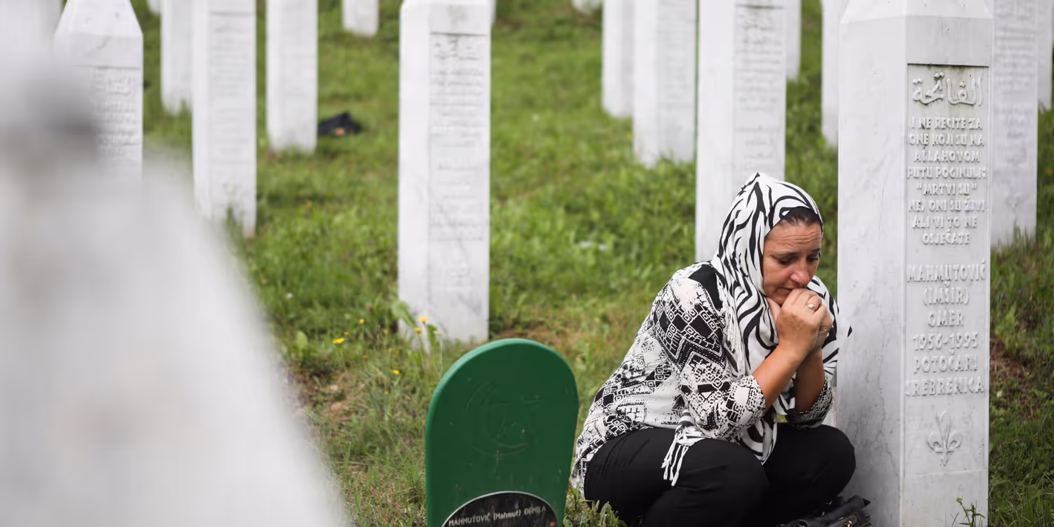 A woman kneels beside a memorial stone at the cemetery in Srebrenica. 