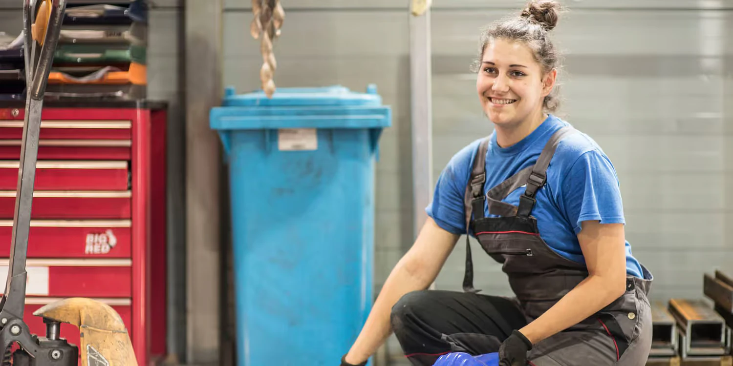 A young woman in a factory smiles at the camera.