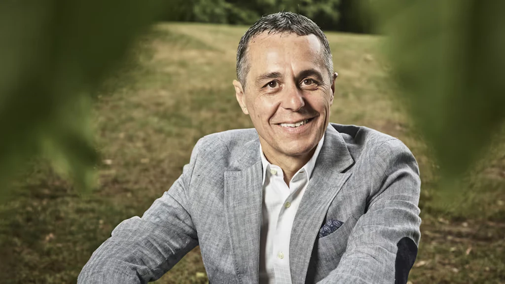 Portrait of Federal Councillor Ignazio Cassis sitting in a meadow. 