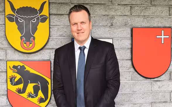 Pascal Sollberger in front of the coats of arms of the cantons of Bern, Schwyz and Uri.