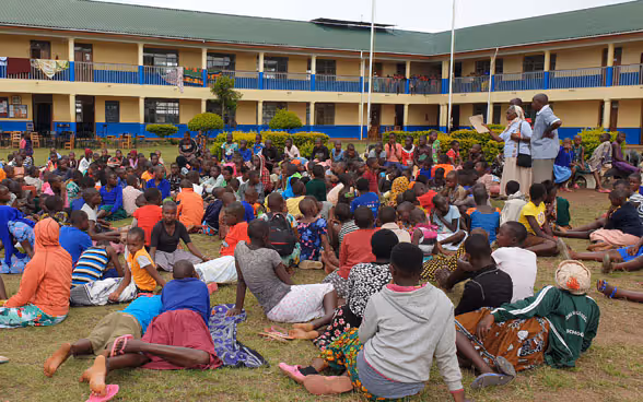 A class of children sit together on a lawn.