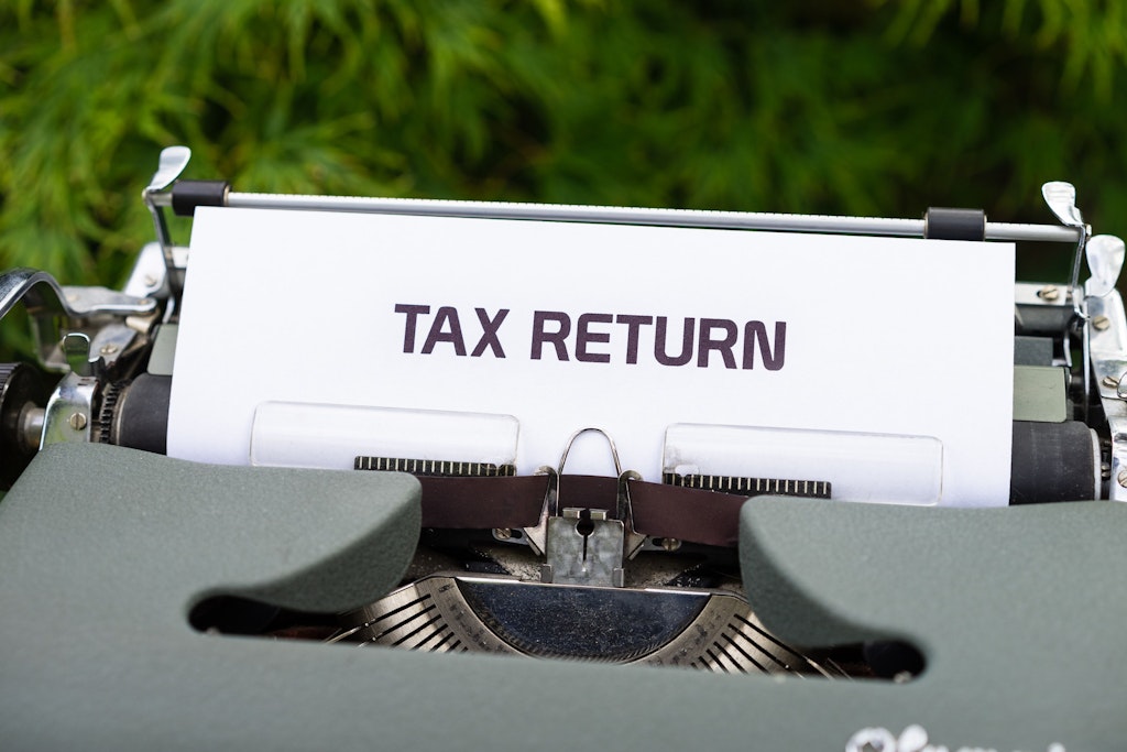 The words TAX RETURN in upper case written on a piece of paper sticking out of a typewriter.