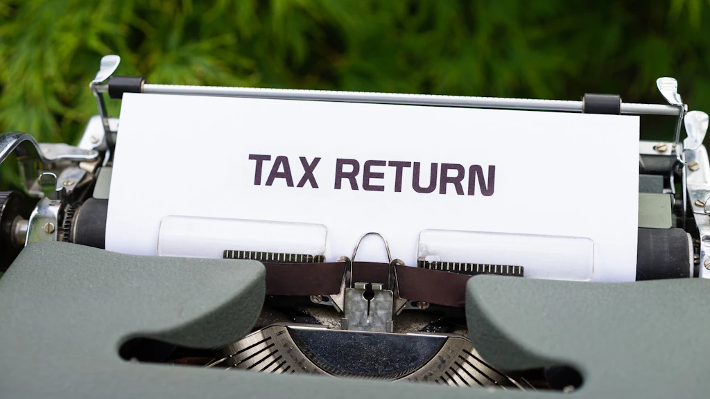 The words TAX RETURN in upper case written on a piece of paper sticking out of a typewriter.