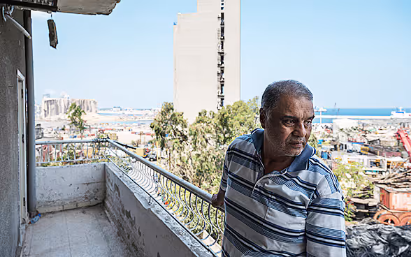 A man stands on the balcony of his broken-down apartment block and looks out over the city. 