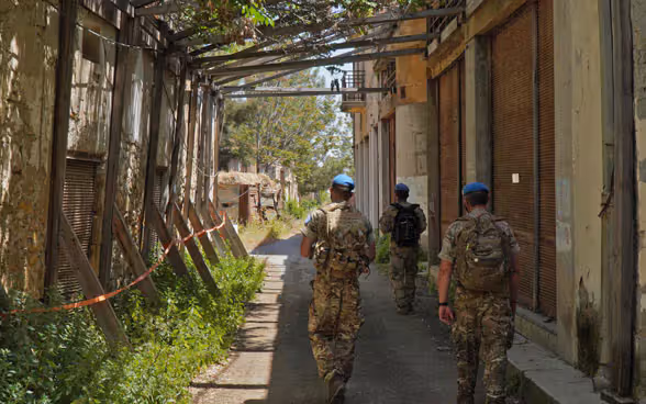 Members of the UN peacekeeping force UNFICYP walk through an alley between dilapidated buildings in the buffer zone.