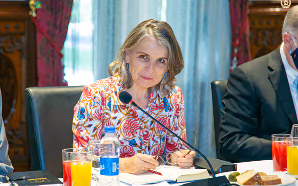 Walburga Roos sitting behind a table in front of a microphone and smiling.