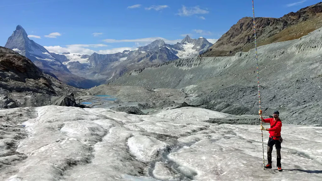 Un homme équipé d’une perche de mesure sur un glacier dans les Alpes suisses.
