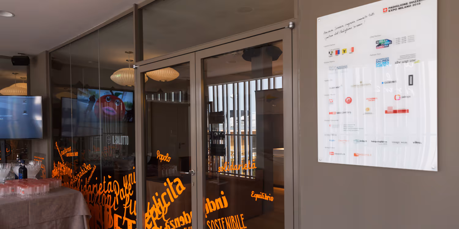 Un panneau blanc située à l’entrée d’un bâtiment détaille l’ensemble des partenaires du pavillon suisse lors de l’Exposition universelle de 2015 à Milan.