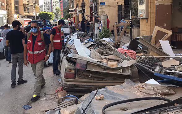 Deux experts du Corps suisse d'aide humanitaire passent devant une voiture démolie.