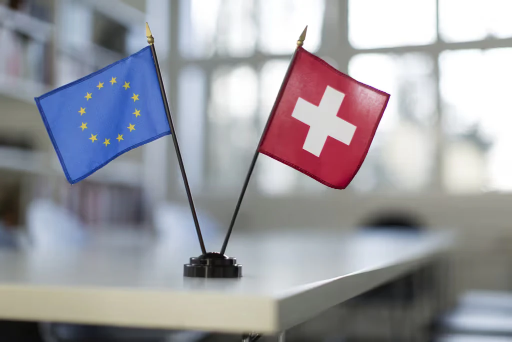 Les drapeaux de la Suisse et de l’UE posés sur une table blanche.