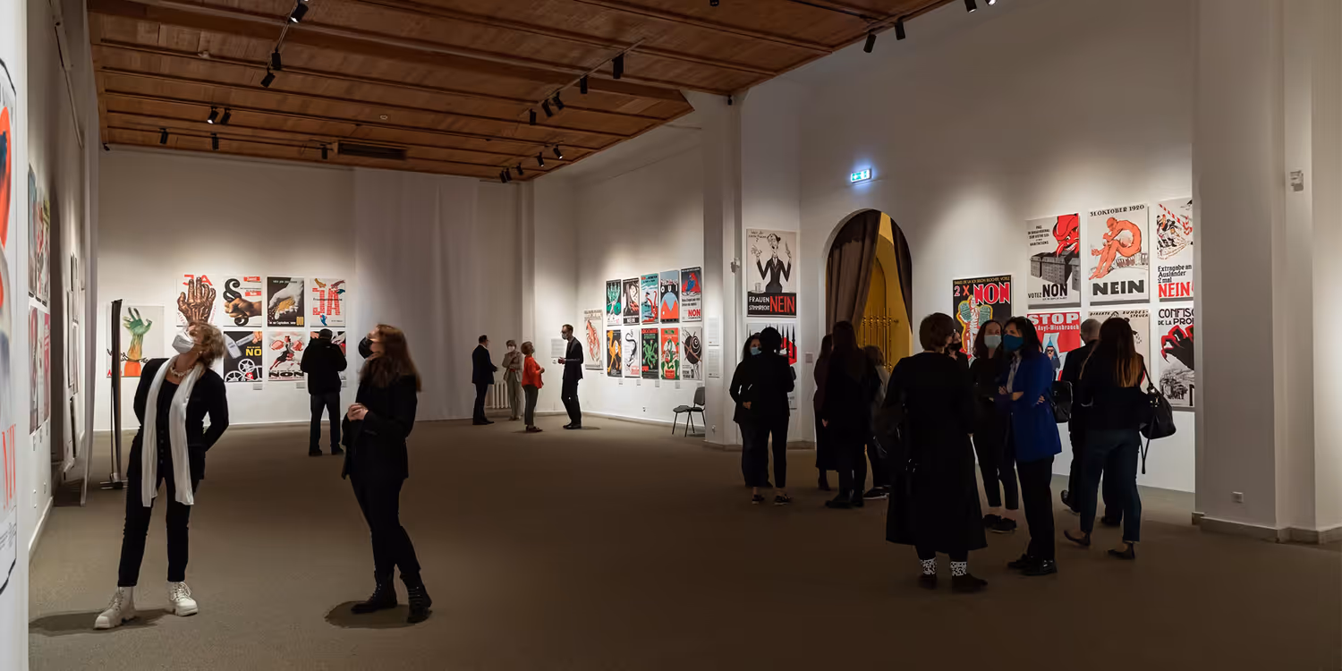 A Vilnius, des visiteurs observent des affiches retraçant 100 ans de votes en Suisse 