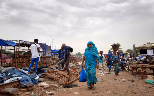 Une femme malienne vêtue d'une robe bleue marche dans une rue avec un sac de provisions.