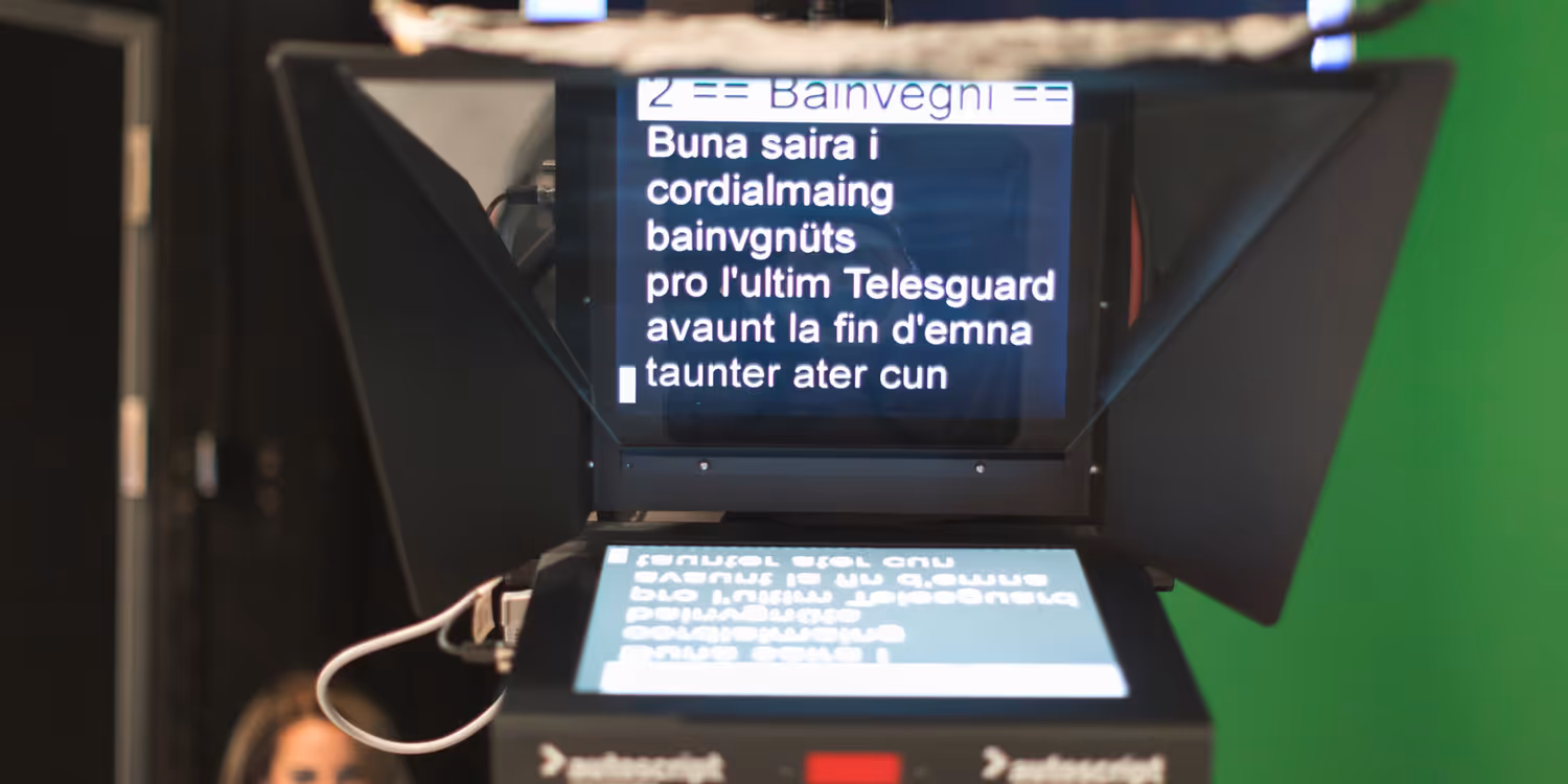 Dans un studio de télévision, un écran affiche le texte du présentateur en romanche.