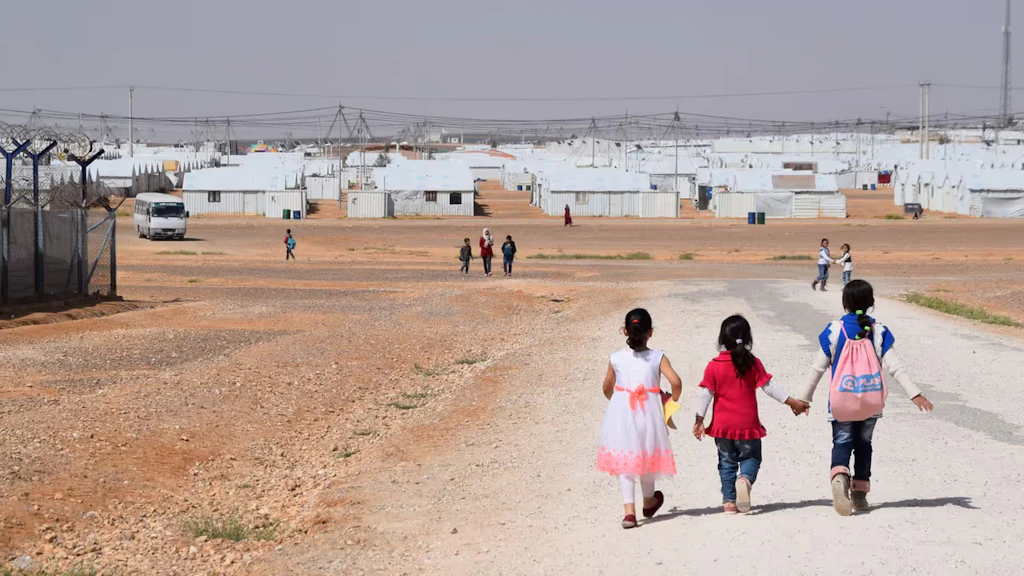 Trois filles marchent sur un chemin de gravier dans le camp de réfugiés d’Azraq, au milieu du désert jordanien.
