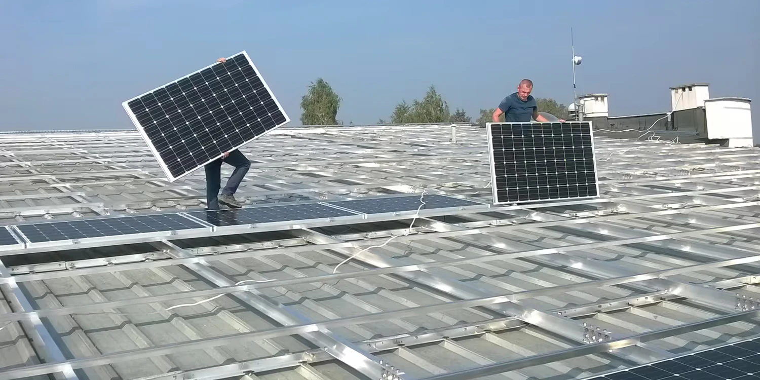 Deux techniciens posent des panneaux photovoltaïques sur le toit d’un bâtiment public.