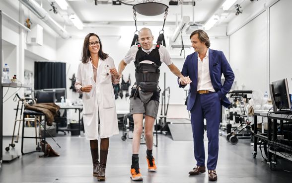 Les professeurs Jocelyne Bloch et Grégoire Courtine traversent une pièce d'un institut de recherche avec Sebastian Tobler, paraplégique.