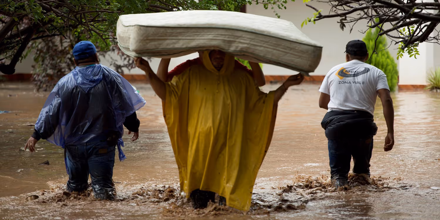 Deux personnes portent un matelas pendant l'inondation. Deux membres du personnel auxiliaire l'accompagnent.