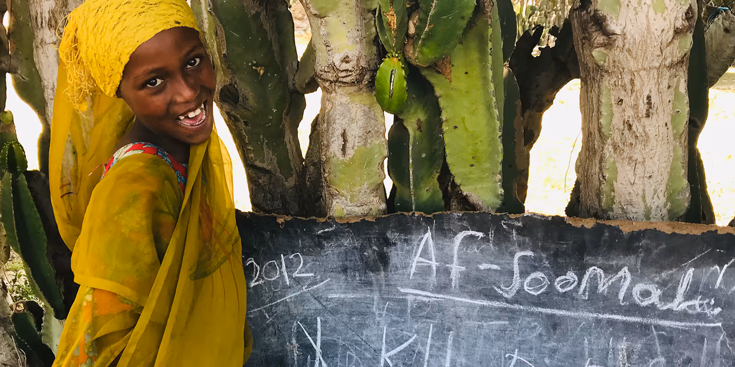 Une fille se tient devant un tableau noir en plein air et regarde dans la caméra (photo prise en Ethiopie) 