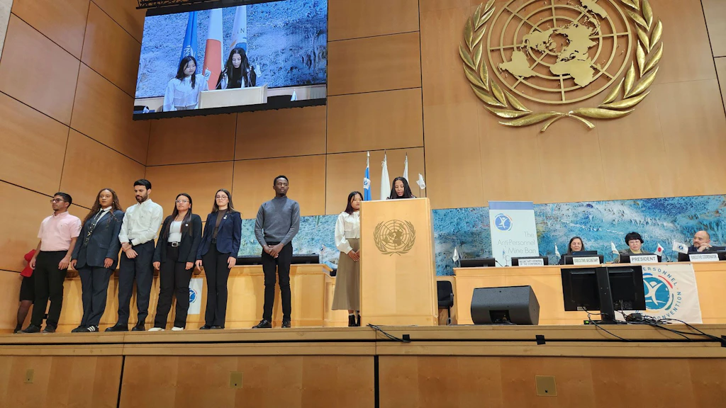Des jeunes engagés dans la lutte contre les mines se tiennent devant un mur sur lequel est apposé le logo de l'ONU.