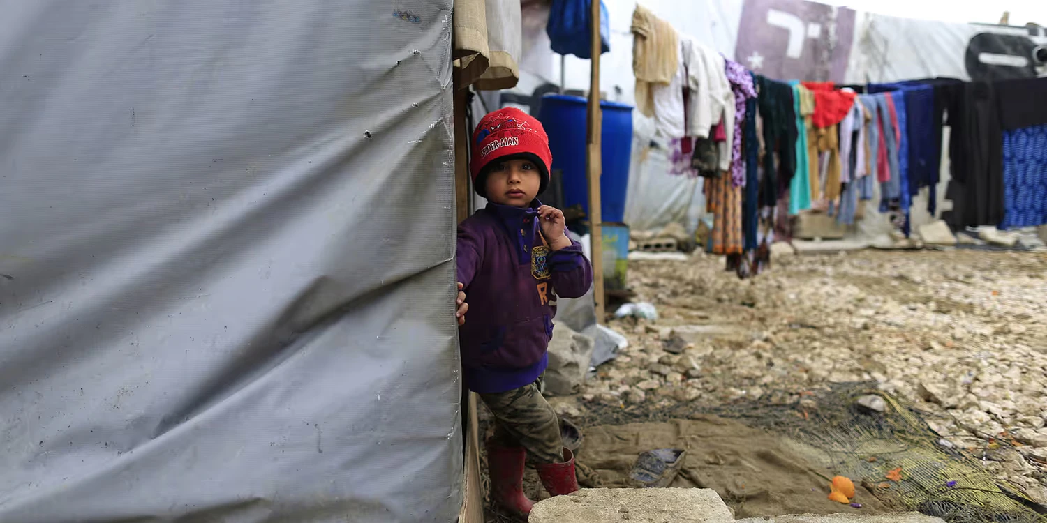 Un jeune réfugié syrien se tient hors de la tente familiale après une pluie battante.