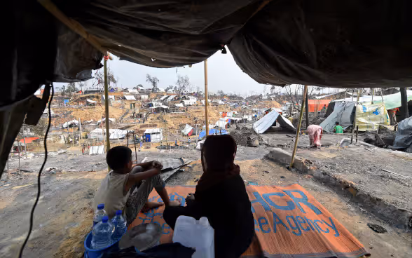Une femme et un enfant sont visibles sur fond d'abris provisoires mis en place pour les réfugiés rohingyas déplacés.