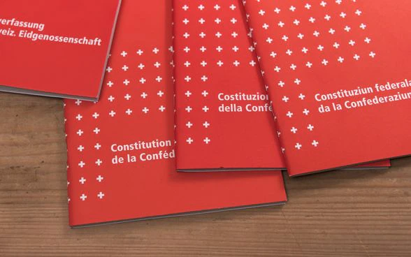 Posés sur un support en bois, quatre exemplaires de la Constitution fédérale suisse dans chacune des langues nationales.
