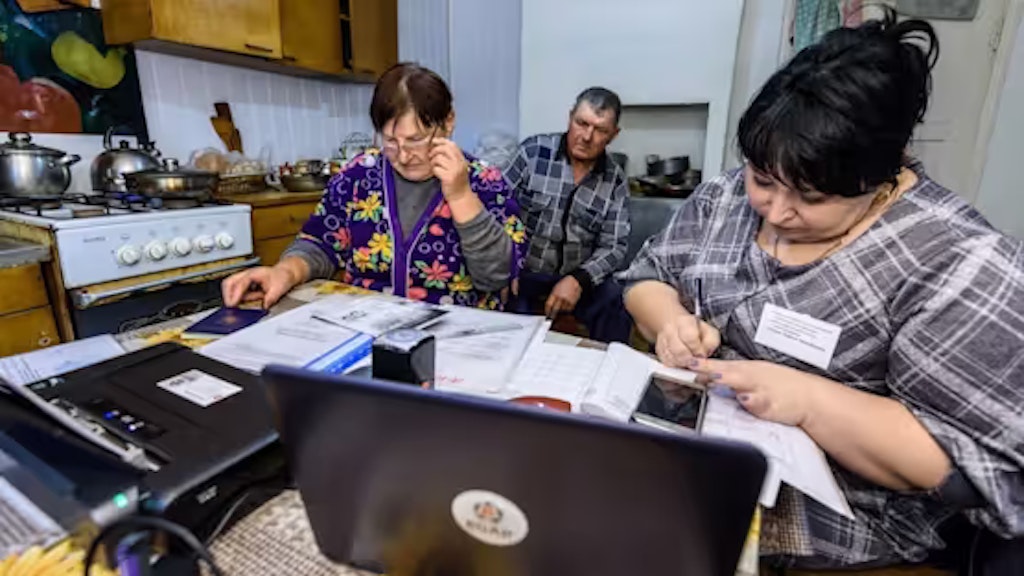 Trois personnes sont assises dans une cuisine en train de travailler sur des documents avec un ordinateur portable.