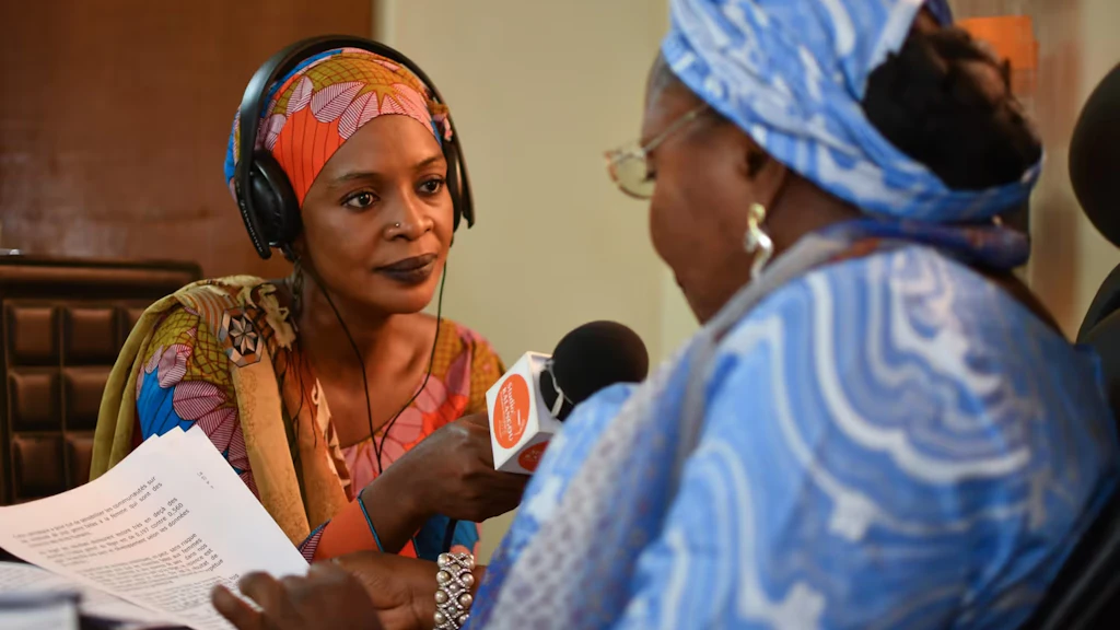 Une femme africaine tend son micro une autre femme dans un studio radio.