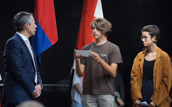 Sur la scène, des étudiantes et des étudiants s’adressent au président de la Confédération Ignazio Cassis.