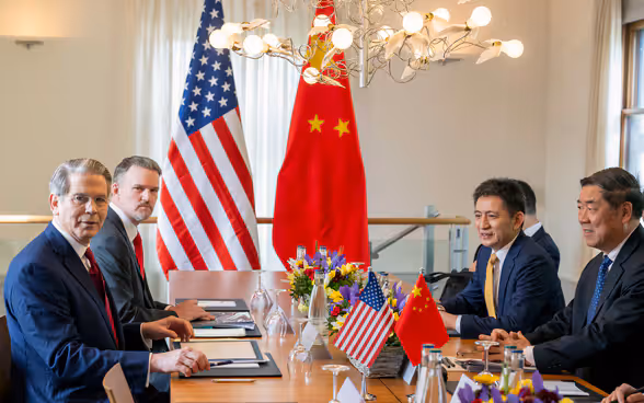 Les délégations des États-Unis et de la Chine assises à la même table, sur fond du drapeau respectif des deux pays.