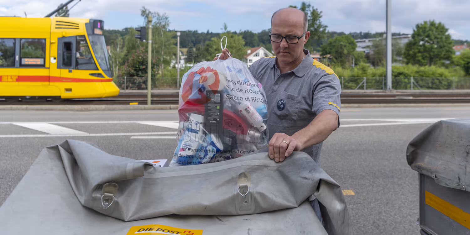 Un facteur met un sac destiné au recyclage rempli de bouteilles en plastique vides et de cartons de boissons dans son chariot. 