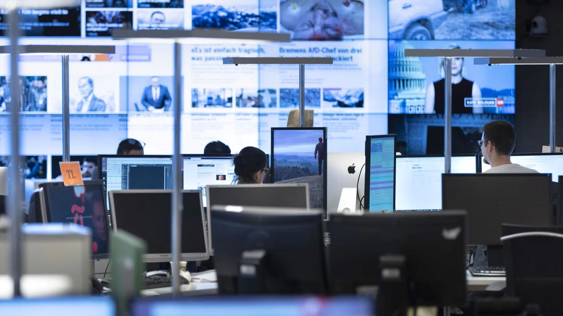 Des professionnels des médias devant leurs écrans dans une salle de rédaction.