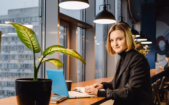 Olha Zajarna est assise à une fenêtre devant un ordinateur portable à la fourre bleu clair.