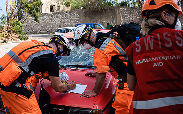 Trois experts du Corps suisse d'aide humanitaire discutent d'un plan d'action sur le capot d'un véhicule en panne.