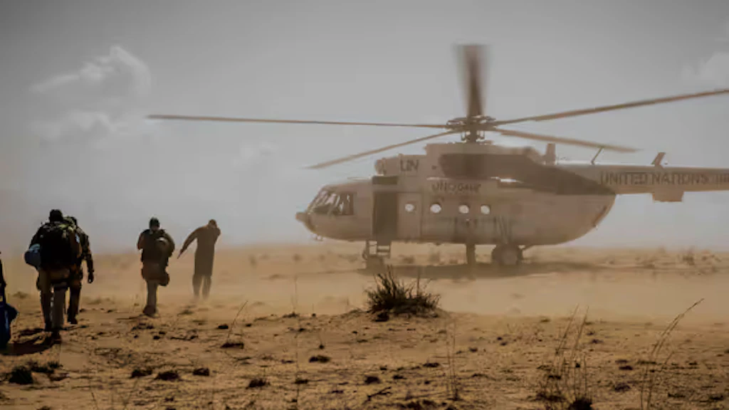 Des personnes courent vers un hélicoptère de l’ONU posé sur un sol de terre, dans le centre du Mali