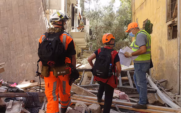 Trois experts du Corps suisse d'aide humanitaire se tiennent devant une maison détruite et entourée de débris.